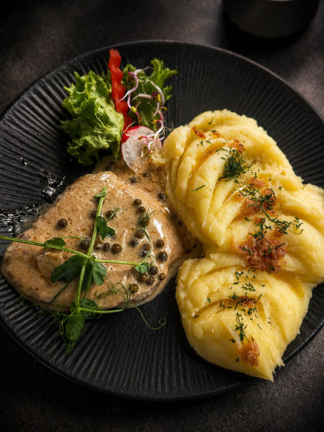 Grillowane mięso z puree i warzywami podane na ciemnym talerzu w Restauracji Fantazja.